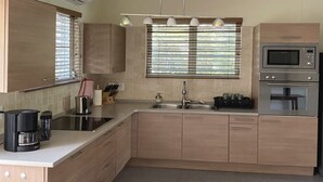 Eine moderne Küche mit eingebautem Herd, Mikrowelle und Spüle. Holzschränke und eine Arbeitsfläche mit Kaffeemaschine und Besteck sind vorhanden.