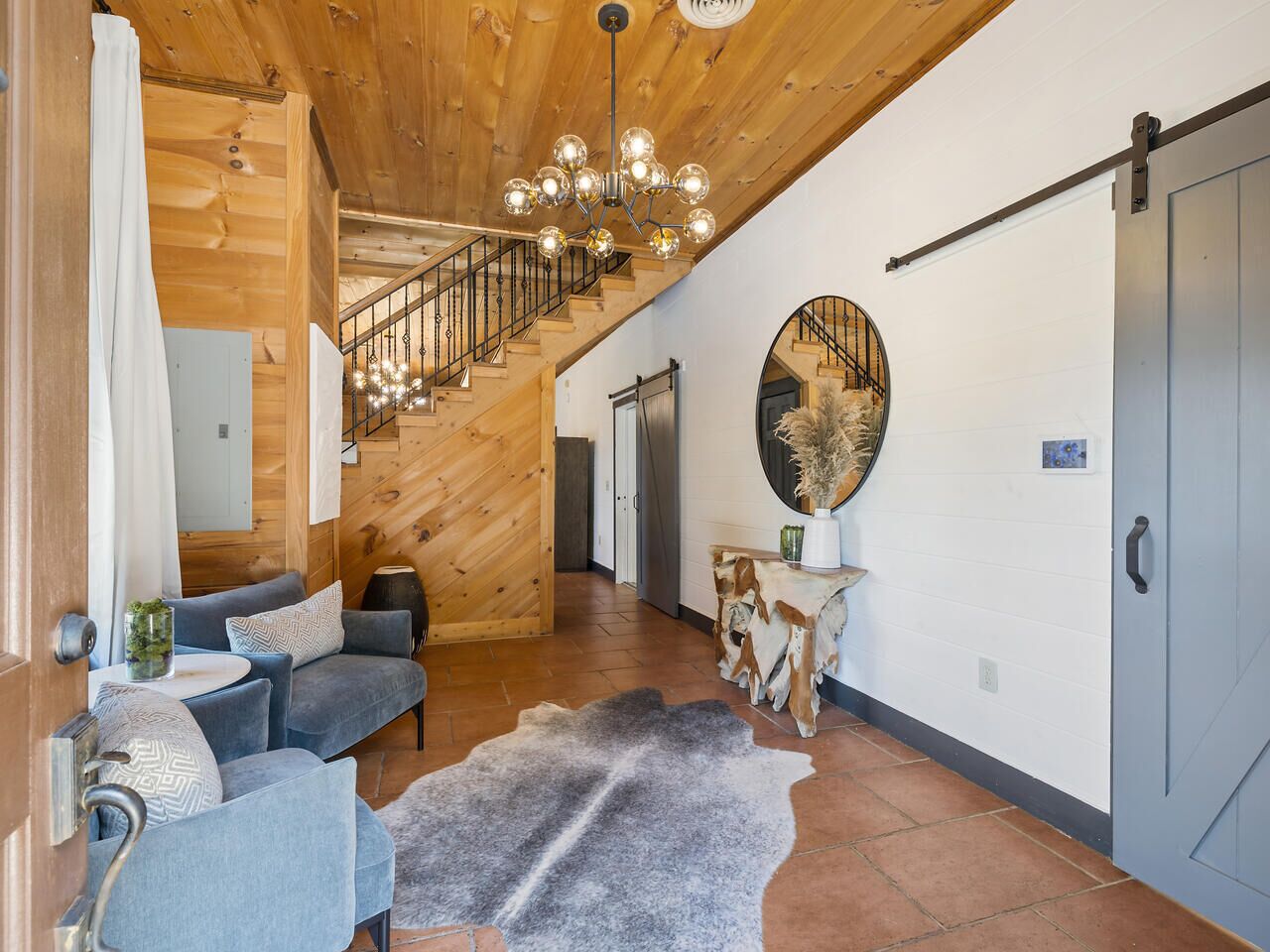 A spacious living area with a wooden staircase, a round mirror, and a rustic rug.