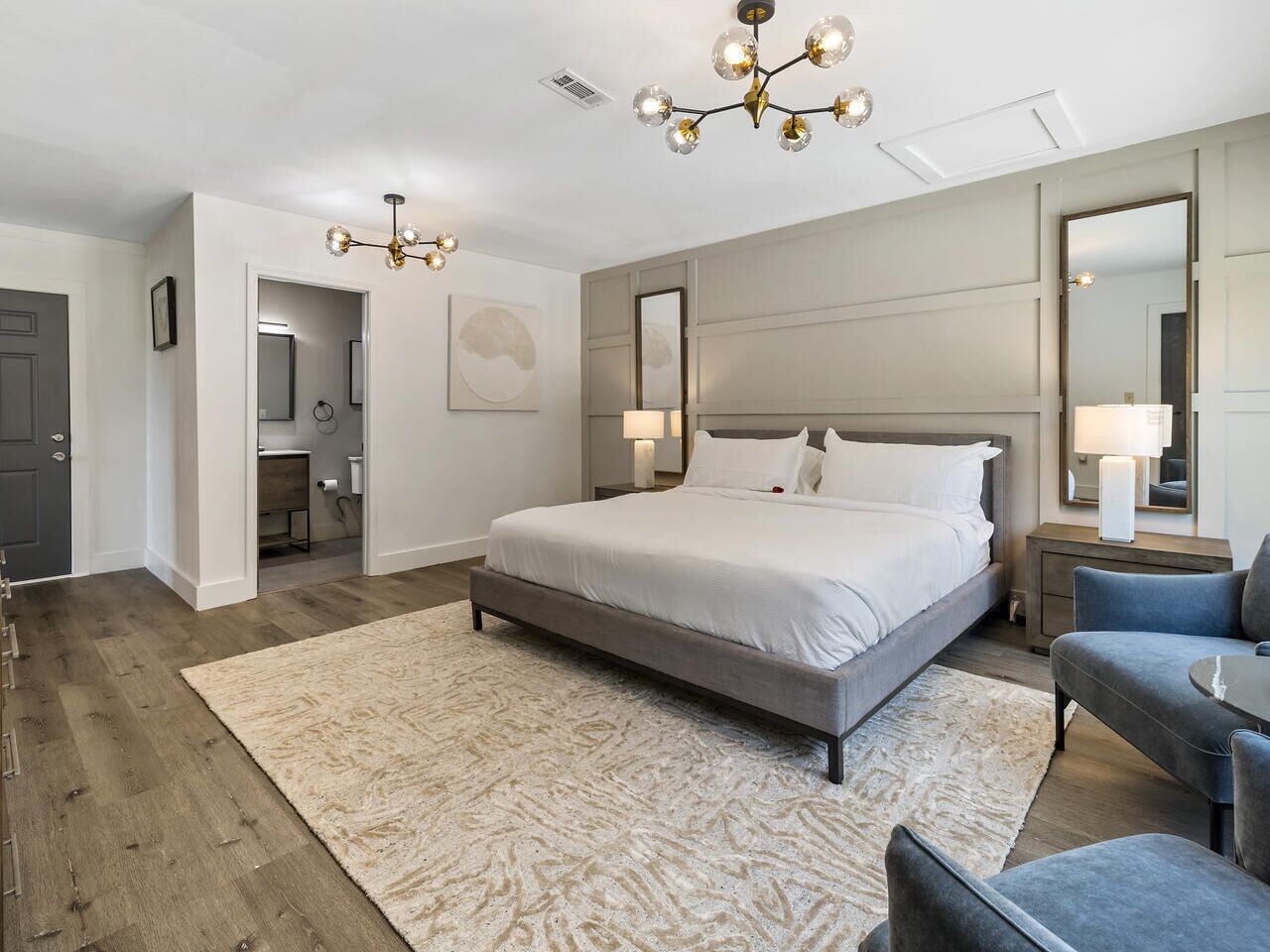 A modern bedroom with a large bed, a chandelier, a desk, and a chair.
