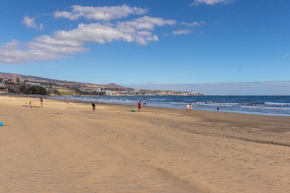 Una extensa playa de arena con gente caminando y descansando.