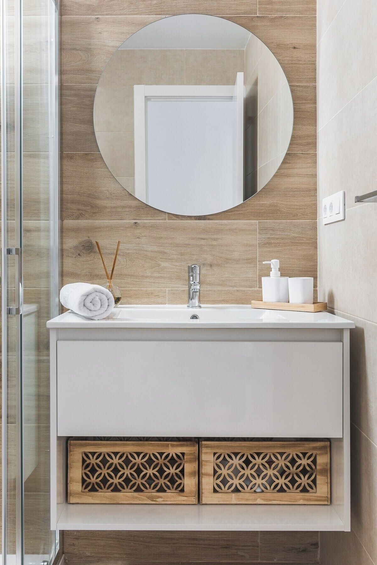 Een badkamer met een witte wastafel, een ronde spiegel en een houten kastje met decoratieve details.