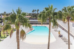 Zona de piscina con palmeras, sillas de descanso y una piscina azul cristalina.
