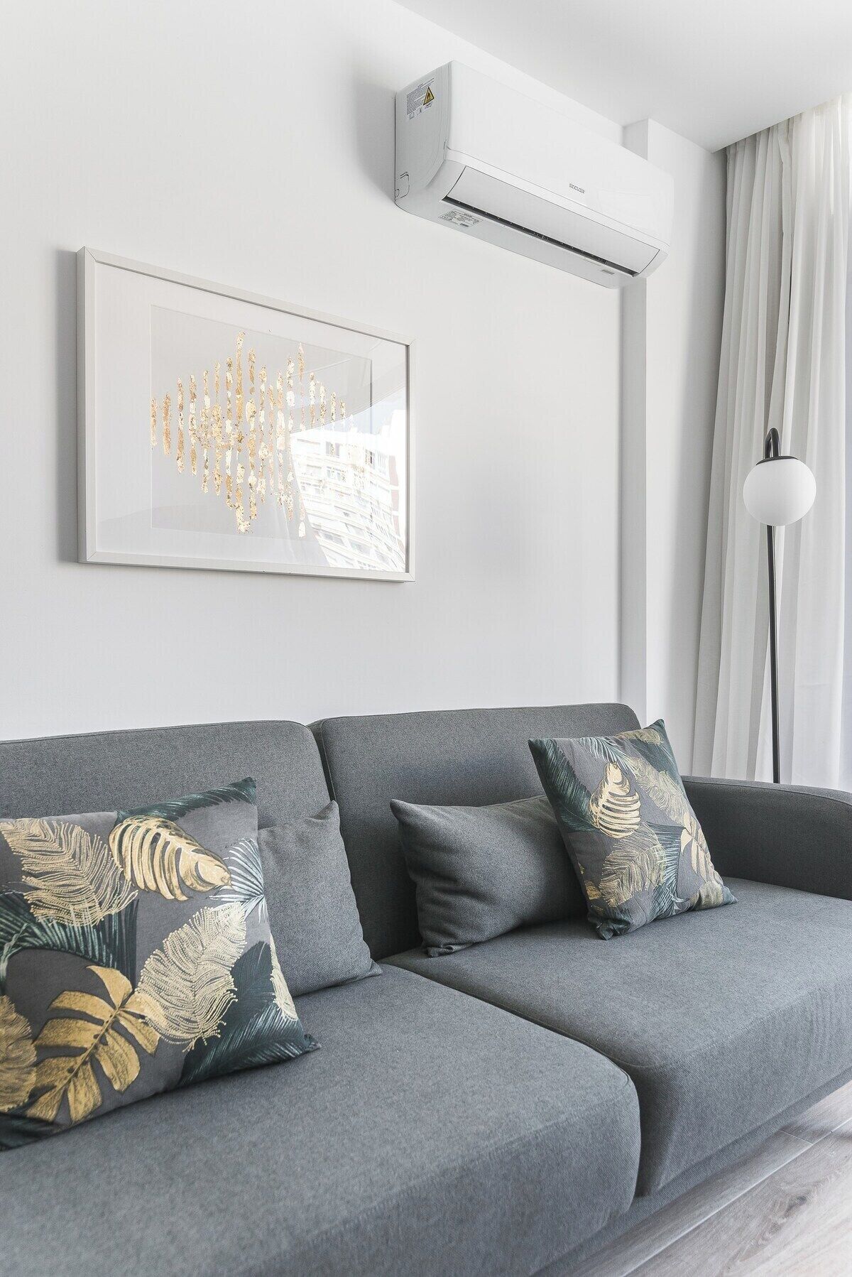 A modern living room with a grey sofa, decorative pillows, a framed artwork, and a ceiling-mounted air conditioner.