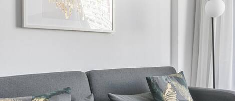 A modern living room with a grey sofa, decorative pillows, a framed artwork, and a ceiling-mounted air conditioner.