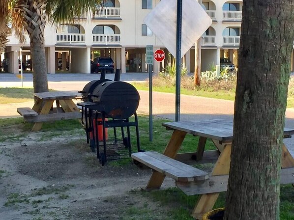 A barbecue grill set up on a picnic table in a grassy area with a stop sign and a building in the background.