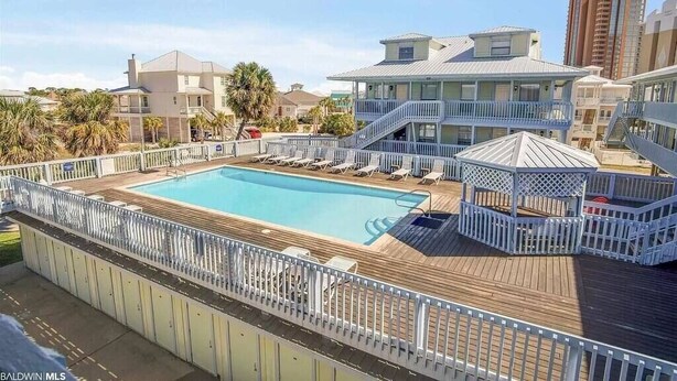 Un espace piscine doté d’une terrasse en bois, de chaises longues et d’un gazebo.