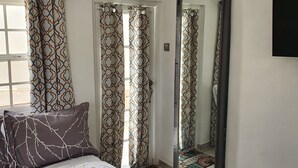 A bedroom with a bed, patterned curtains, a sliding door, and a mirror. - Devachan Apartments (Worthing)