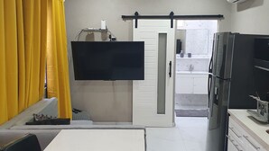 A compact kitchen with a refrigerator, microwave, and a flat-screen TV mounted on the wall. - Devachan Apartments (Worthing)