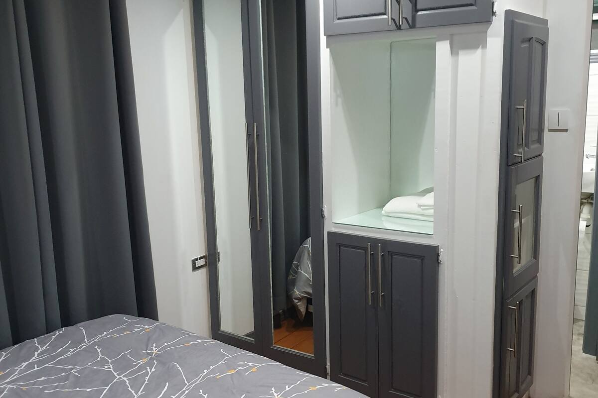 Une chambre à coucher avec un lit, une armoire grise à plusieurs portes et un miroir.