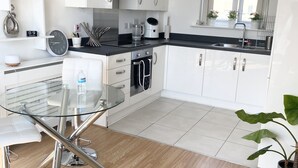 Una cocina moderna con armarios blancos, una encimera negra y una mesa de comedor de vidrio.