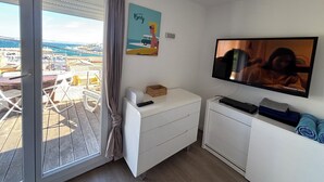 Habitación con puerta corrediza de vidrio, televisión de pantalla plana, un mueble blanco pequeño y un cuadro en la pared.