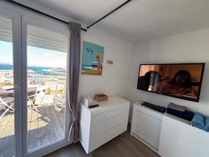 Ein Zimmer mit einer Schiebetür, einem Flachbildfernseher, einer kleinen weißen Kommode und einem Bild an der Wand.