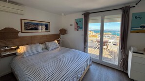Un dormitorio con cama, una mesita de noche, lámpara, ventana con cortinas y vista a la ciudad.