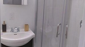 Un bagno con un lavandino bianco, mobili scuri, uno specchio e un box doccia in vetro.