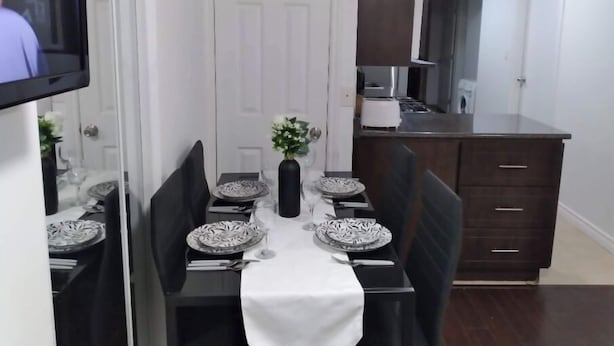 Zona pranzo con tavolo apparecchiato per quattro, una TV a muro e una cucina sullo sfondo.