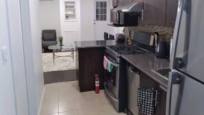 Una cucina compatta con mobili in legno scuro, elettrodomestici in acciaio inossidabile e un piccolo angolo ristoro con tavolo e sedie in vetro.