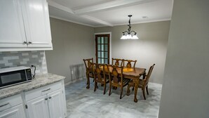 Une cuisine avec des meubles blancs, un plan de travail en granit, une table à manger avec des chaises et un lustre.