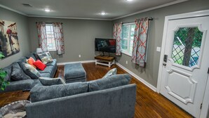 Un salon avec un canapé gris, un téléviseur et une porte dotée d’une fenêtre.