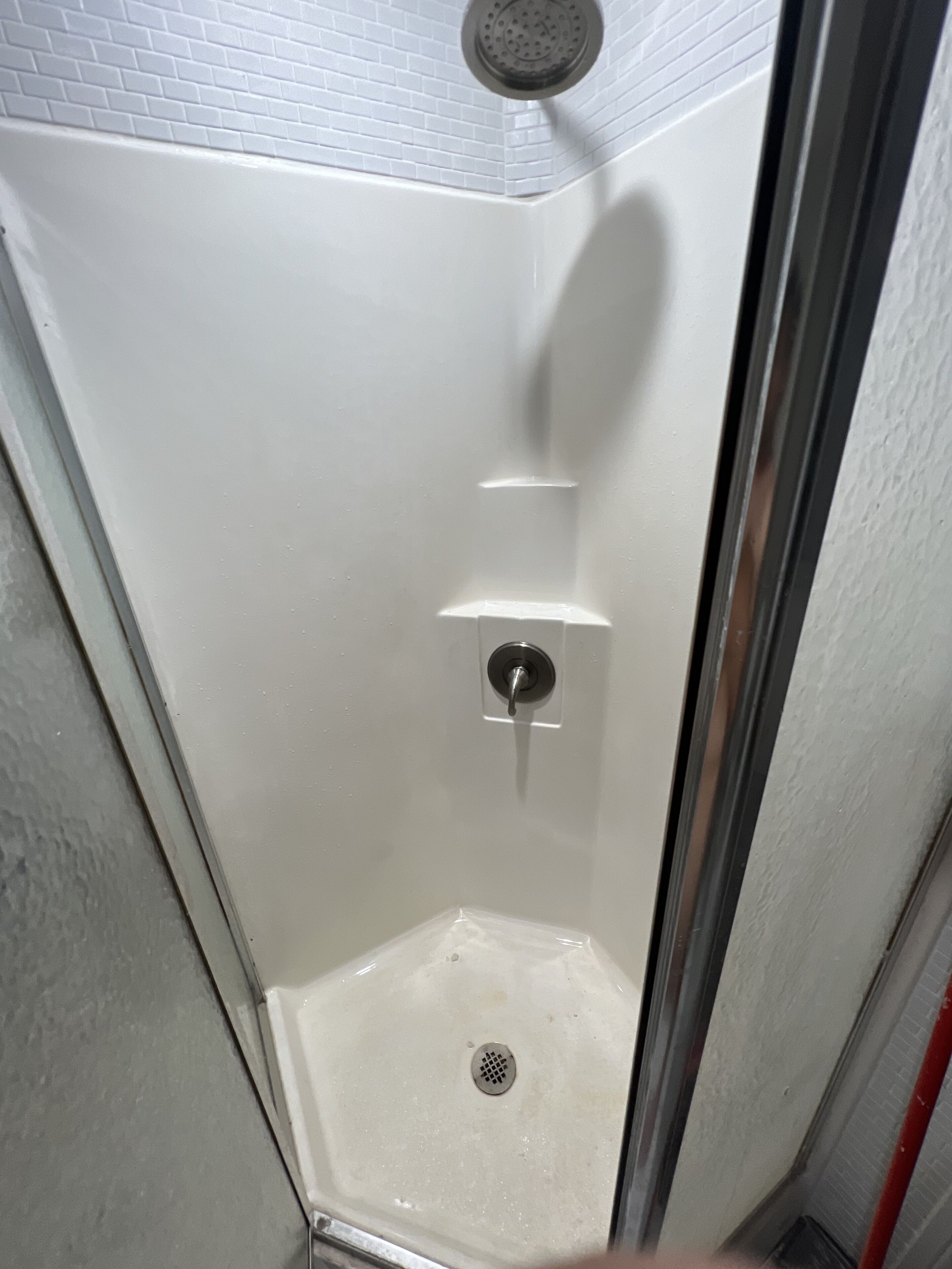 A small, enclosed shower area with a white tiled wall, a showerhead, and a drain.
