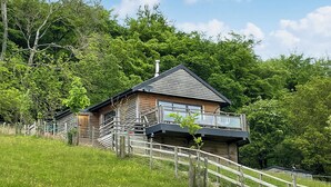 A wooden cabin with a balcony, surrounded by a wooden fence and lush greenery. - Offa's Dyke Lodge - UK10835 (Stanner, near Kington)