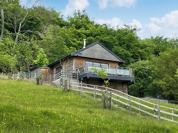 A wooden cabin with a balcony, surrounded by a wooden fence and lush greenery.