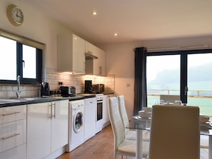 A modern kitchen with a washing machine, a coffee maker, and a dining area with a view. - Offa's Dyke Lodge - UK10835 (Stanner, near Kington)