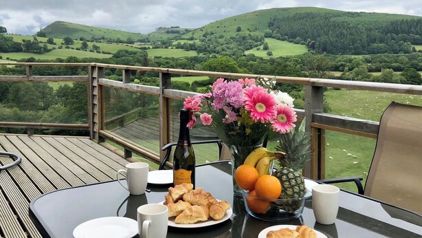 A table with croissants, a bottle of prosecco, a vase of flowers, and a bowl of fruit on a balcony overlooking a green landscape. - Offa's Dyke Lodge - UK10835 (Stanner, near Kington)