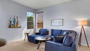 A modern living room with a blue sectional sofa, a round coffee table, a floor lamp, and artwork on the walls.