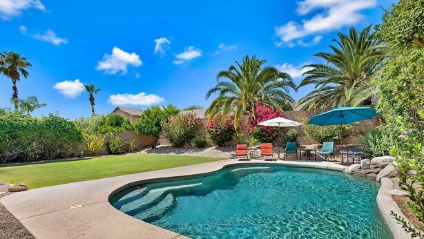 A swimming pool with a curved edge, surrounded by a well-maintained lawn and various plants.
