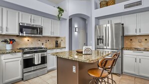 A modern kitchen with white cabinetry, stainless steel appliances, a granite countertop, and a bar stool.
