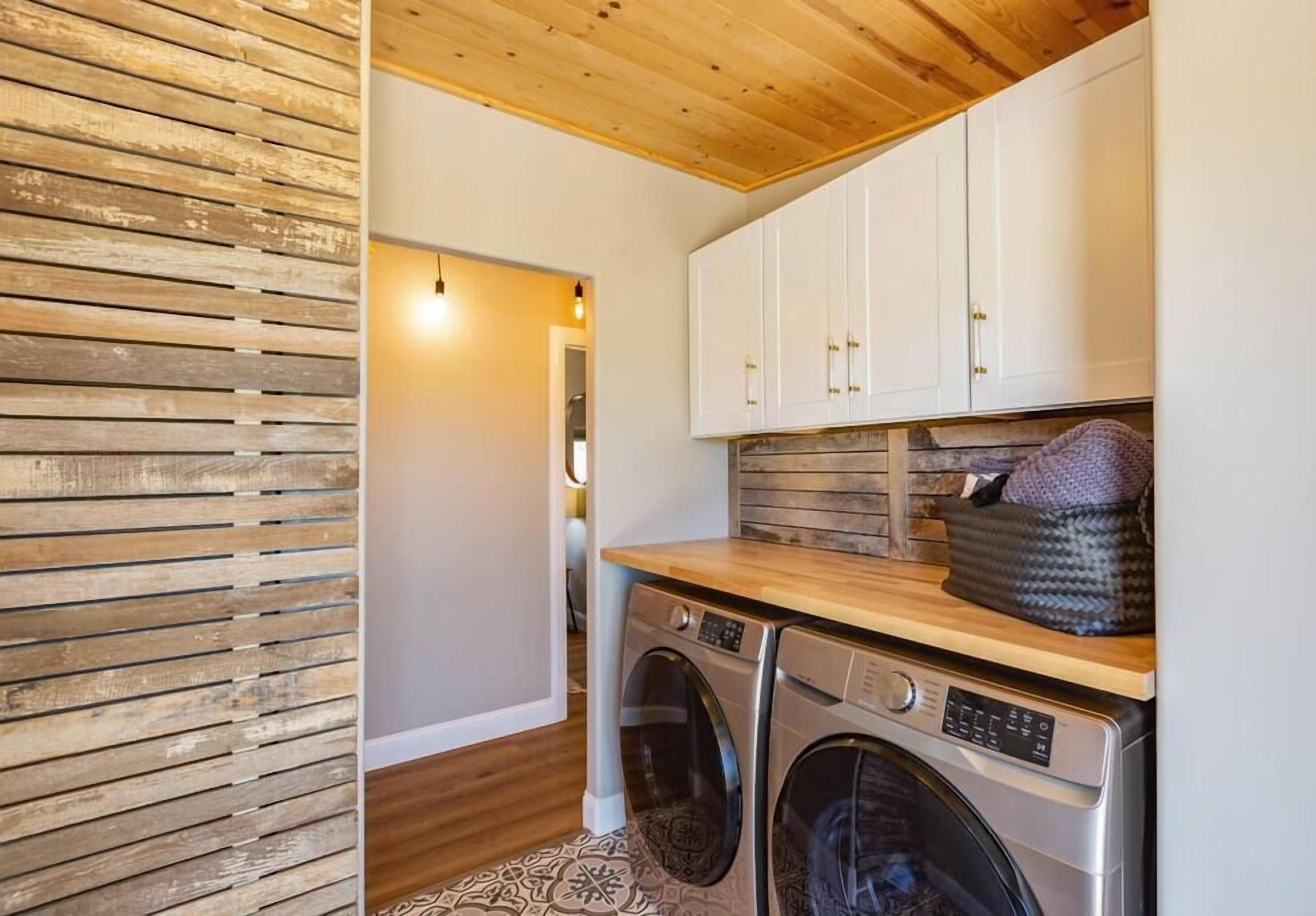 A laundry room with two washing machines, wooden cabinets, and a patterned rug.