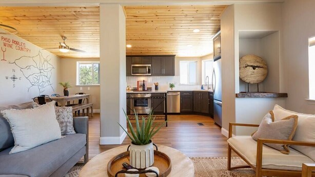 A modern living room with a grey sofa, a wooden coffee table with a plant, and a large wooden ceiling. - Casa Caballo: Vineyard views and close to downtown (Paso Robles)