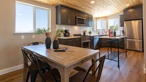 A modern kitchen with dark cabinets, stainless steel appliances, and a wooden dining table with chairs. - Casa Caballo: Vineyard views and close to downtown (Paso Robles)