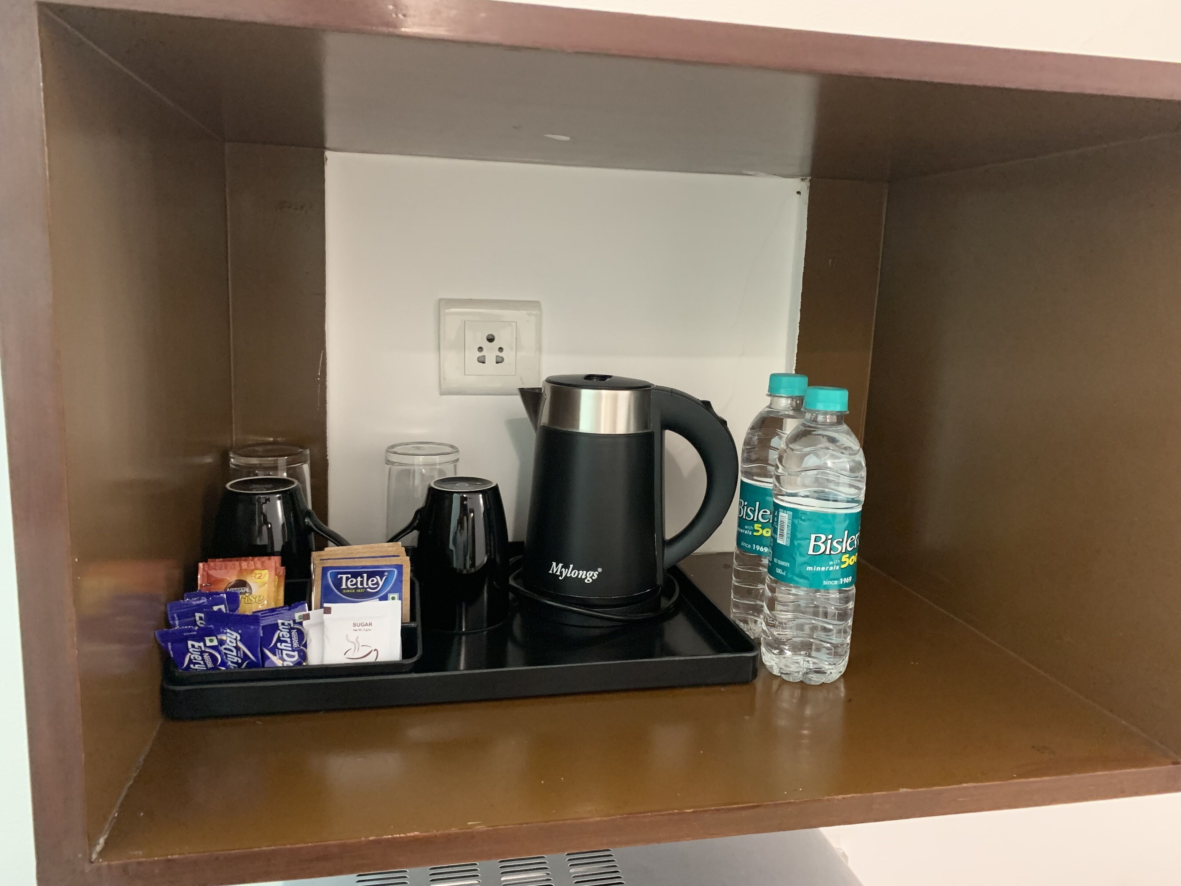 A kitchenette with a coffee maker, water bottles, a kettle, a sugar packet, and a chocolate bar.