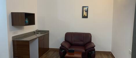 A compact living space with a kitchenette, a brown leather sofa, and a small wooden table.