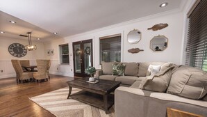 Ein Wohnzimmer mit Sofa, Sesseln, Couchtisch und einer Uhr an der Wand.