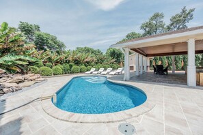 A swimming pool with a curved edge, surrounded by lounge chairs and a covered patio area. - Pool & Hot Tub in Backyard Oasis! Mins to Beach & Biloxi! Sleeps 6! (Gulfport)