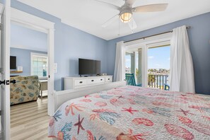 Een slaapkamer met een bed, een plafondventilator, een televisie en een balkon met uitzicht.
