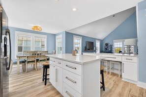 Une cuisine moderne avec des meubles blancs, un grand îlot central et un coin repas comprenant des chaises et une table en bois.