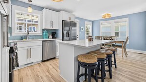 Une cuisine moderne avec des meubles blancs, des appareils en acier inoxydable et un îlot central doté de tabourets de bar.
