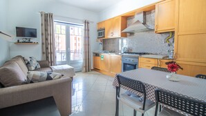A compact living space with a sofa, dining table, kitchen area, and a TV mounted on the wall.