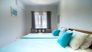 A room with two beds, a window with curtains, a painting on the wall, and a wooden headboard.