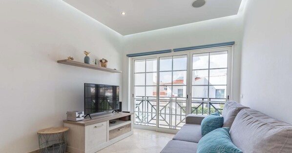 Un salon moderne avec un téléviseur à écran plat posé sur un meuble en bois, un canapé agrémenté de coussins à motifs et un balcon doté d’une balustrade.