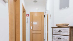 A hallway with wooden doors, a white wall, a ceiling light, and a small wooden cabinet with drawers. - #104 Fanichi Flat by Home Holidays (Albufeira)