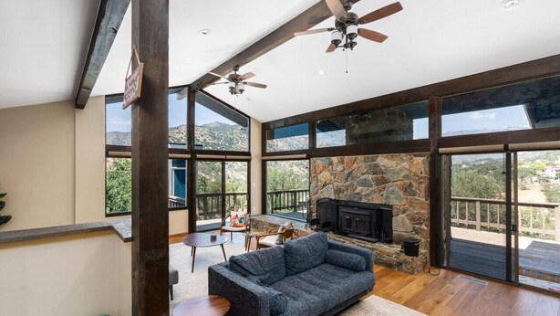 A spacious living area with a stone fireplace, large windows, and a ceiling fan. - Mtn View, Hot Tub, Open Kitchen, 10m to Sequoia (Three Rivers)