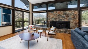 A spacious living room with a stone fireplace, large windows, and a view of the mountains. - Mtn View, Hot Tub, Open Kitchen, 10m to Sequoia (Three Rivers)