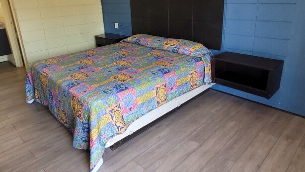 A bedroom with a bed, wooden flooring, a blue accent wall, and a small shelf. - Relax inn (Lucedale)