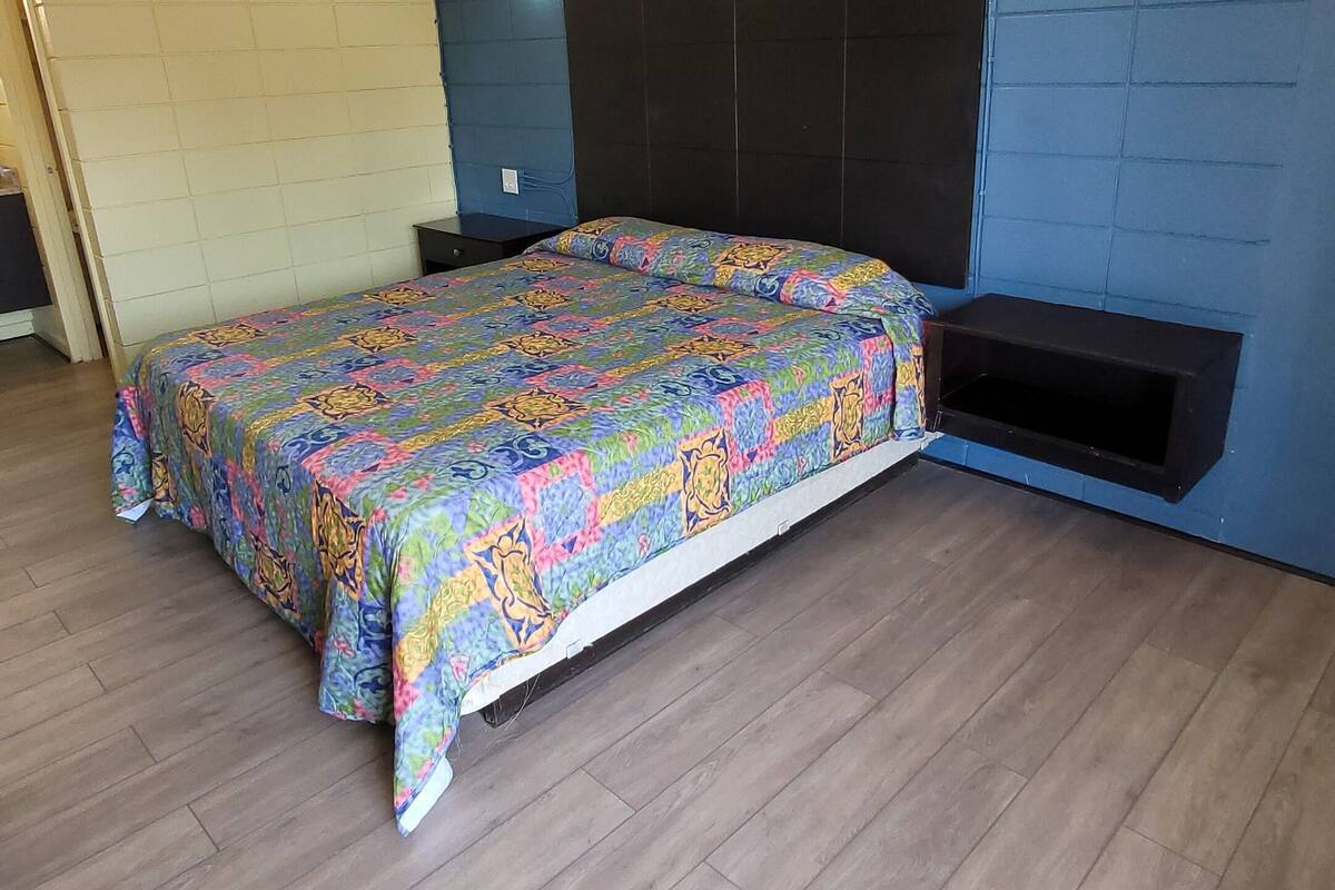 A bedroom with a bed, wooden flooring, a blue accent wall, and a small shelf.