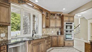 A kitchen with wooden cabinets, a stone backsplash, and a built-in oven. - Exceptional Getaway for Family & Friends (Rush City)
