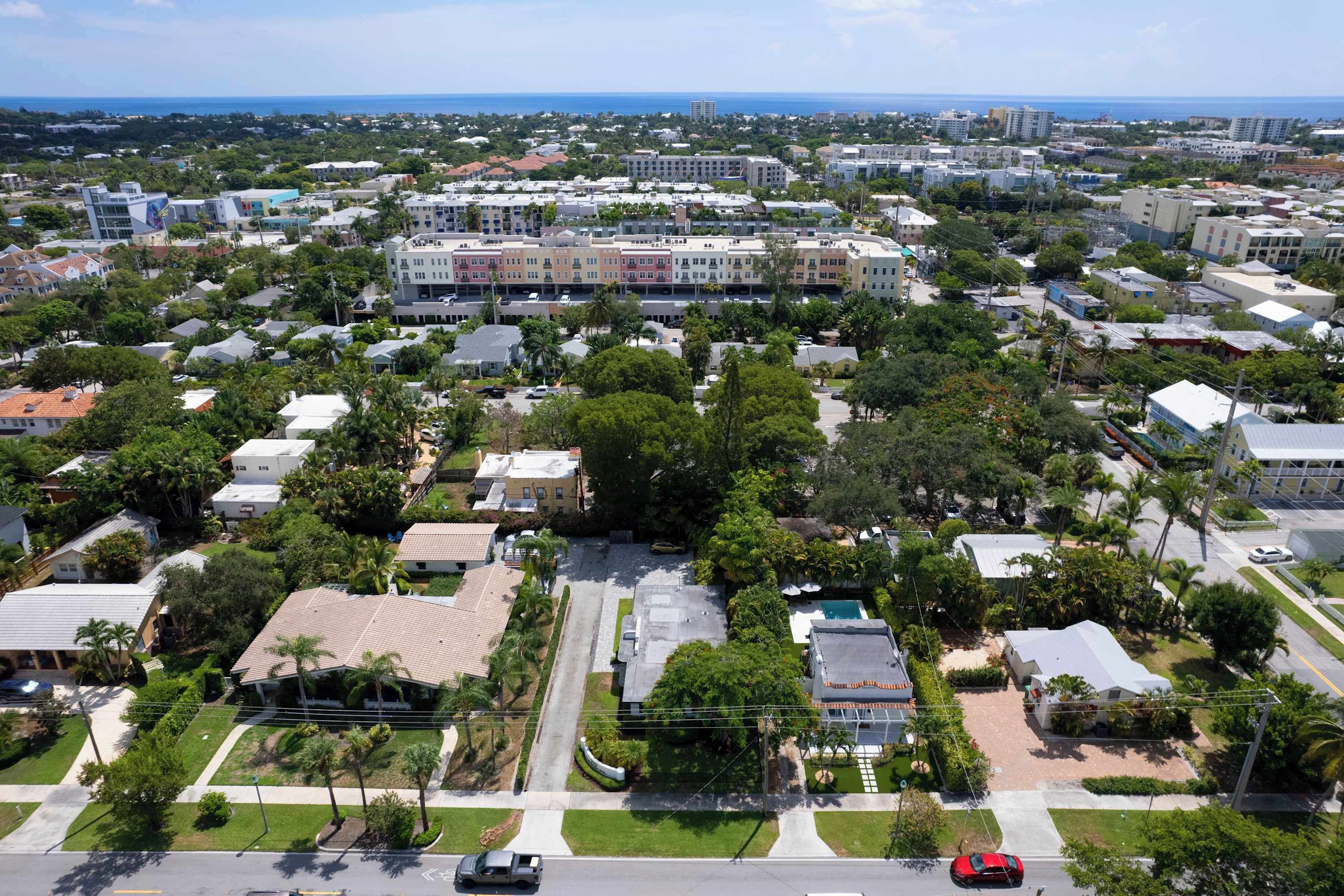 Vista aérea de una zona residencial con casas unifamiliares y edificios de apartamentos, rodeada de vegetación y una vista despejada del océano.